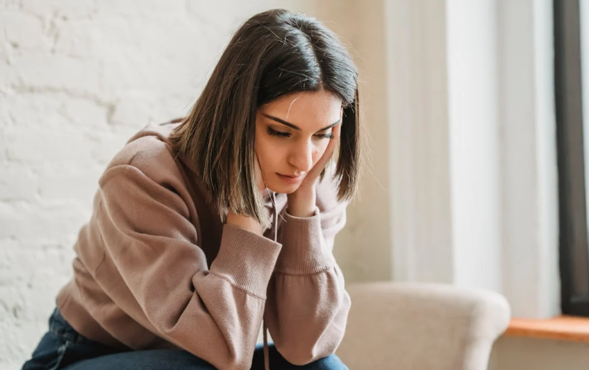 upset woman, sad woman, trauma, woman staring at floor, brunette, woman on couch