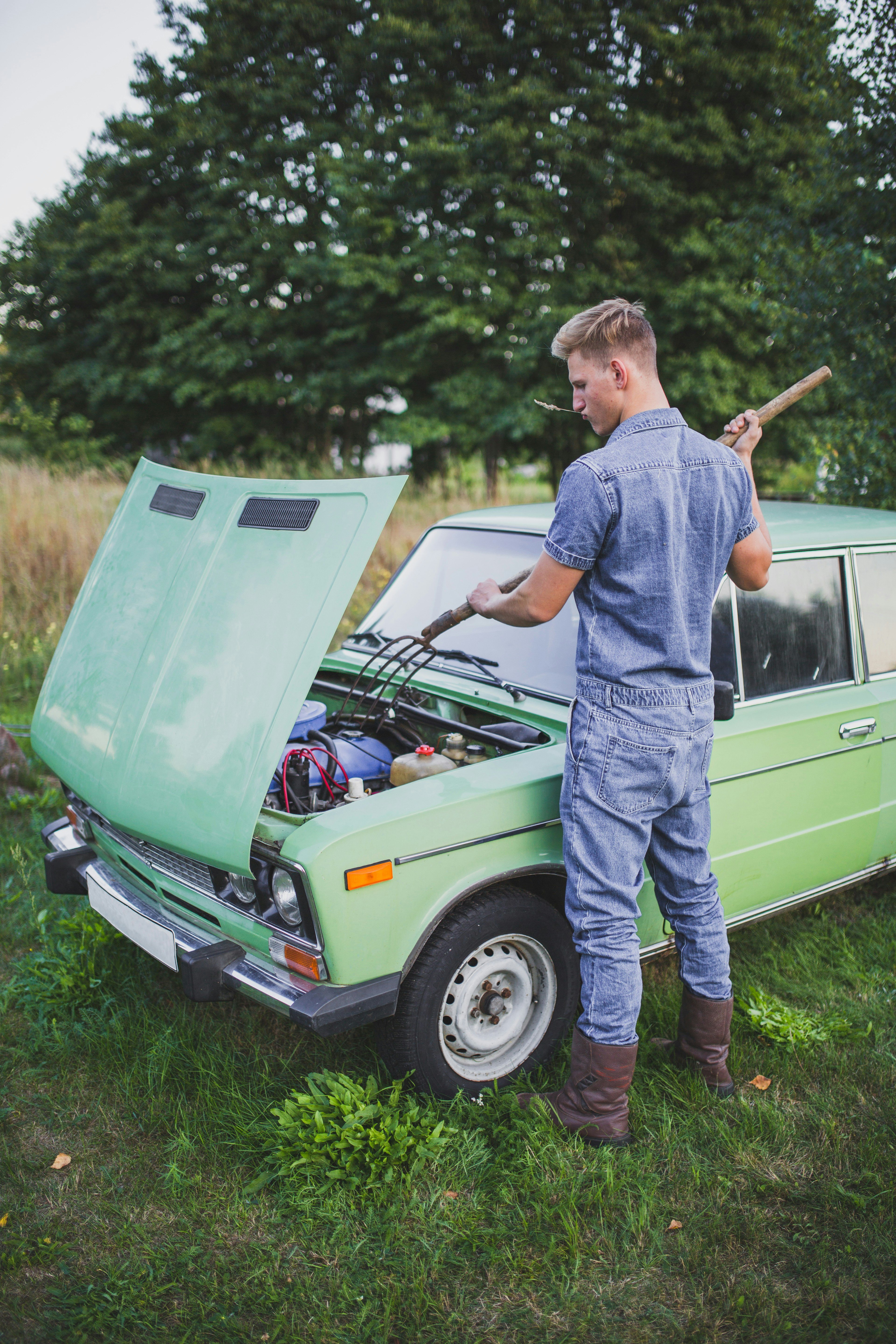 A man stands over an open hood of a green car