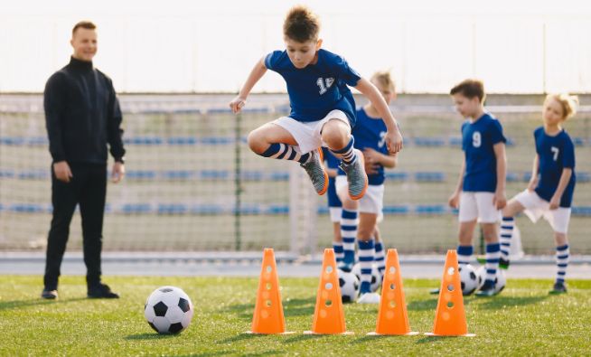 A child jumps over cones playing soccer.