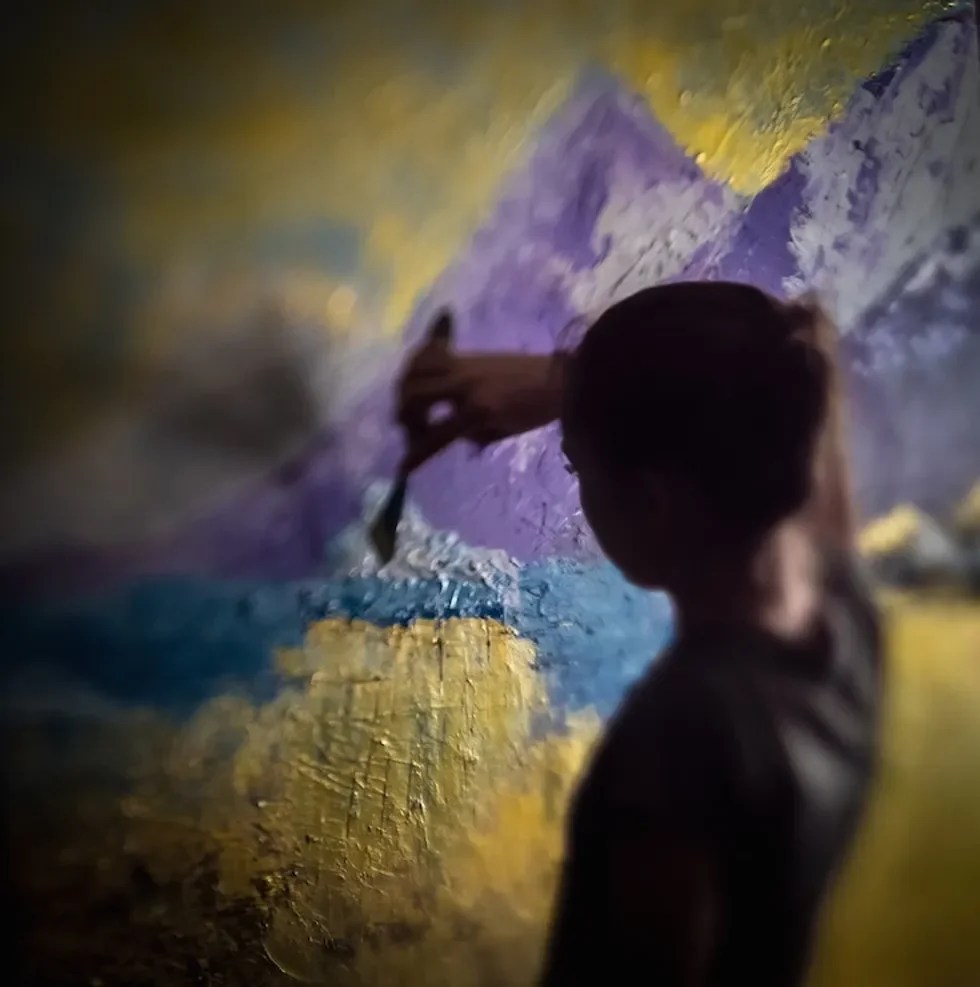 Silhouette of a person painting a colorful landscape with mountains.