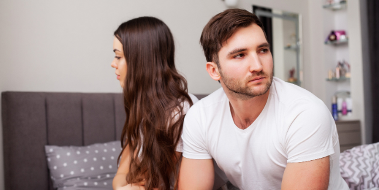 A man and woman sit on a bed facing away from each other