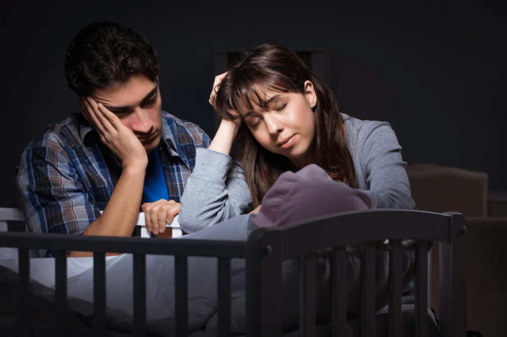 A man and woman look over their newborn baby in a crib