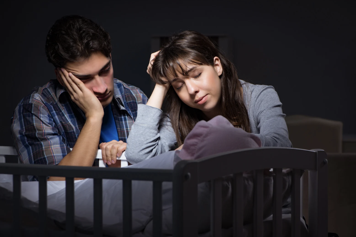 A man and woman look over their newborn baby in a crib