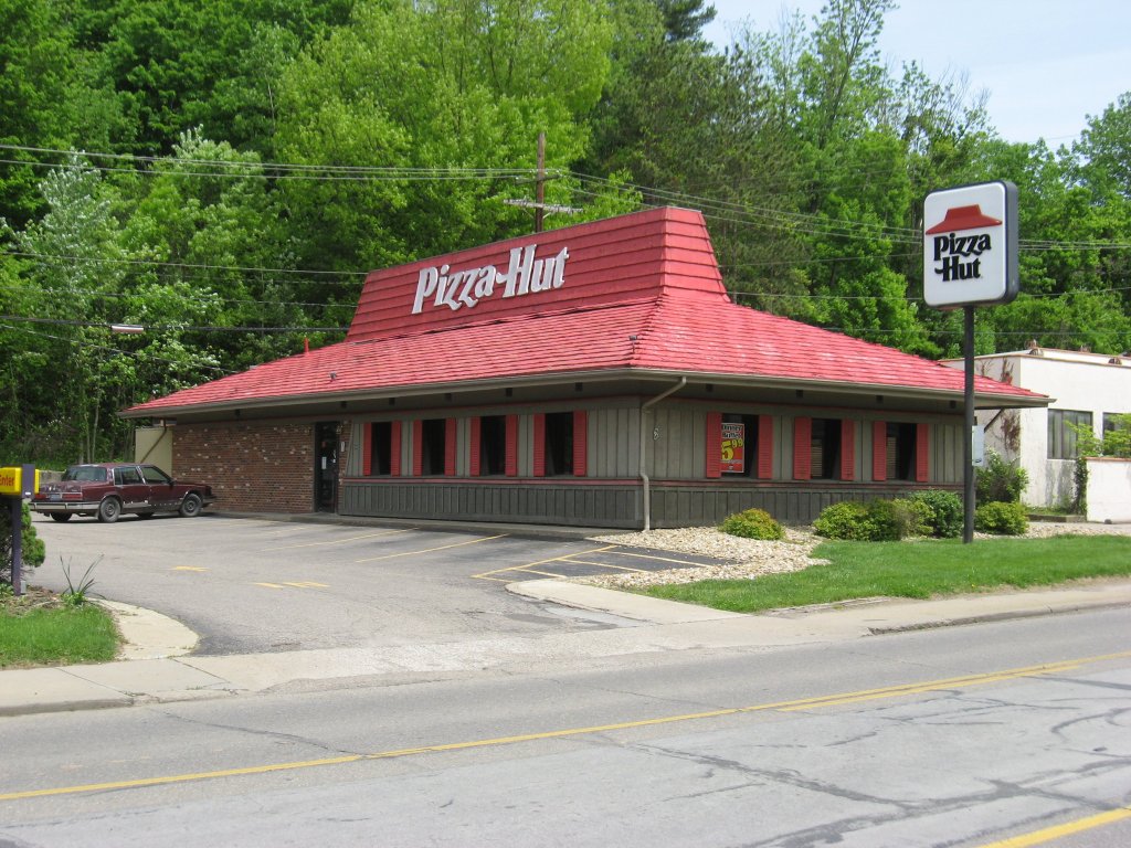 A classic Pizza Hut restaurant with a red roof and surrounding greenery.