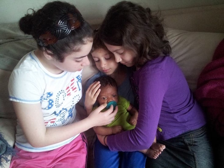 Three children hold a baby
