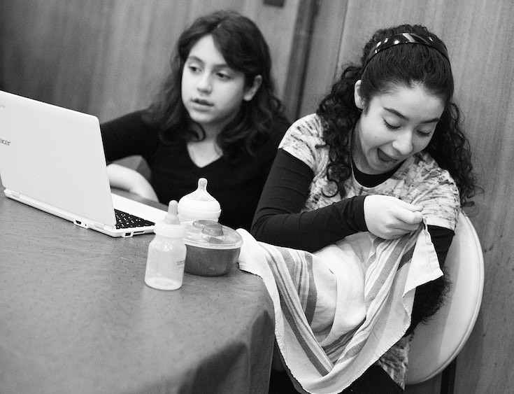 Two young girls with a laptop, bottles, and a baby.
