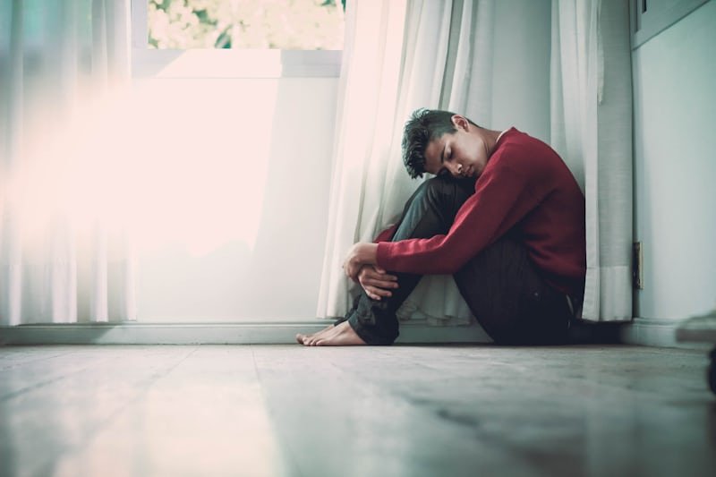 teen boy curled up in a corner of a room
