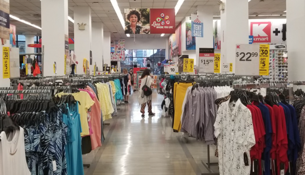 woman stands in department store aisle surrounded by racks of clothes