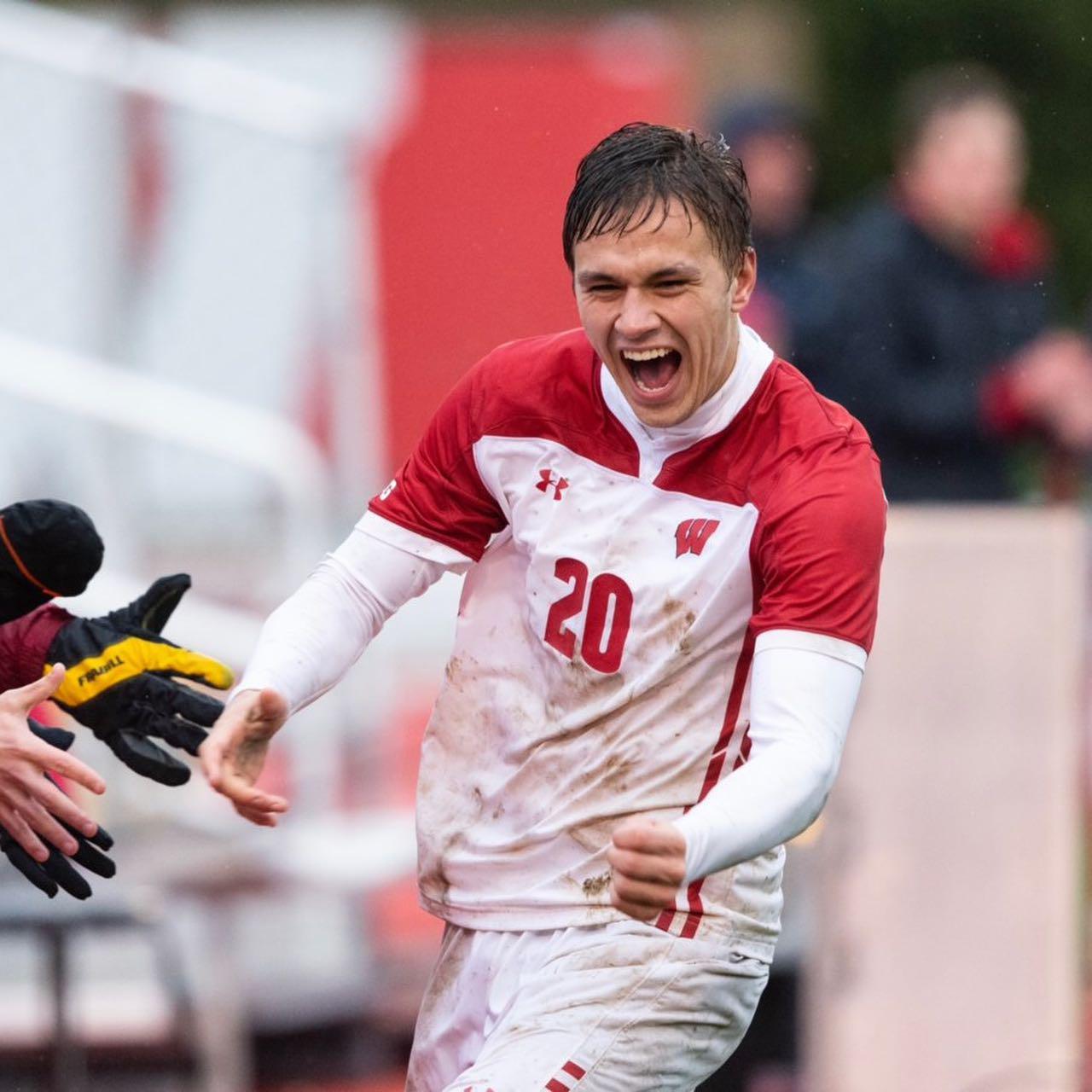 Noah Melick open mouth smile, fist pump by his side. White and red soccer uniform