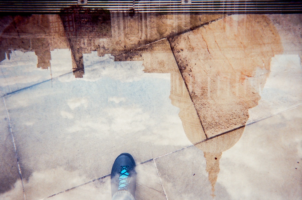 reflection of a building in a puddle beside a blue shoe