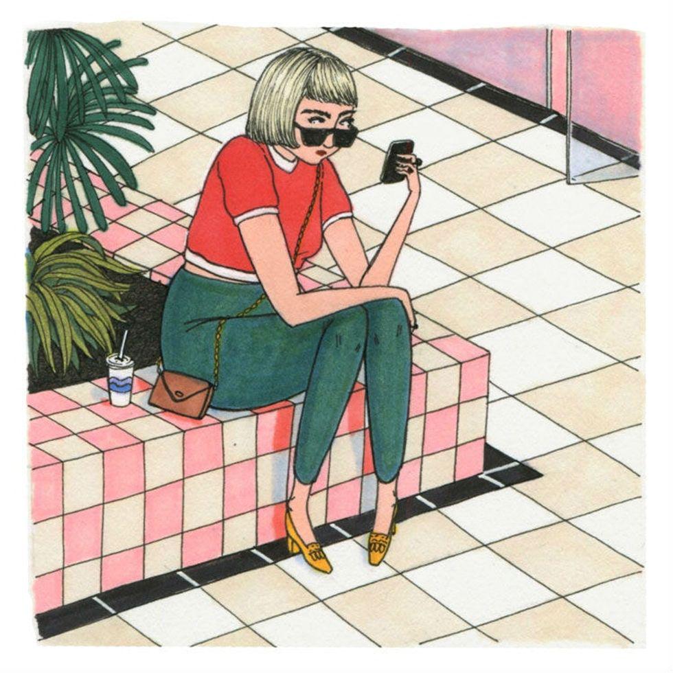 woman sits on a bench and stares at her phone in a mall