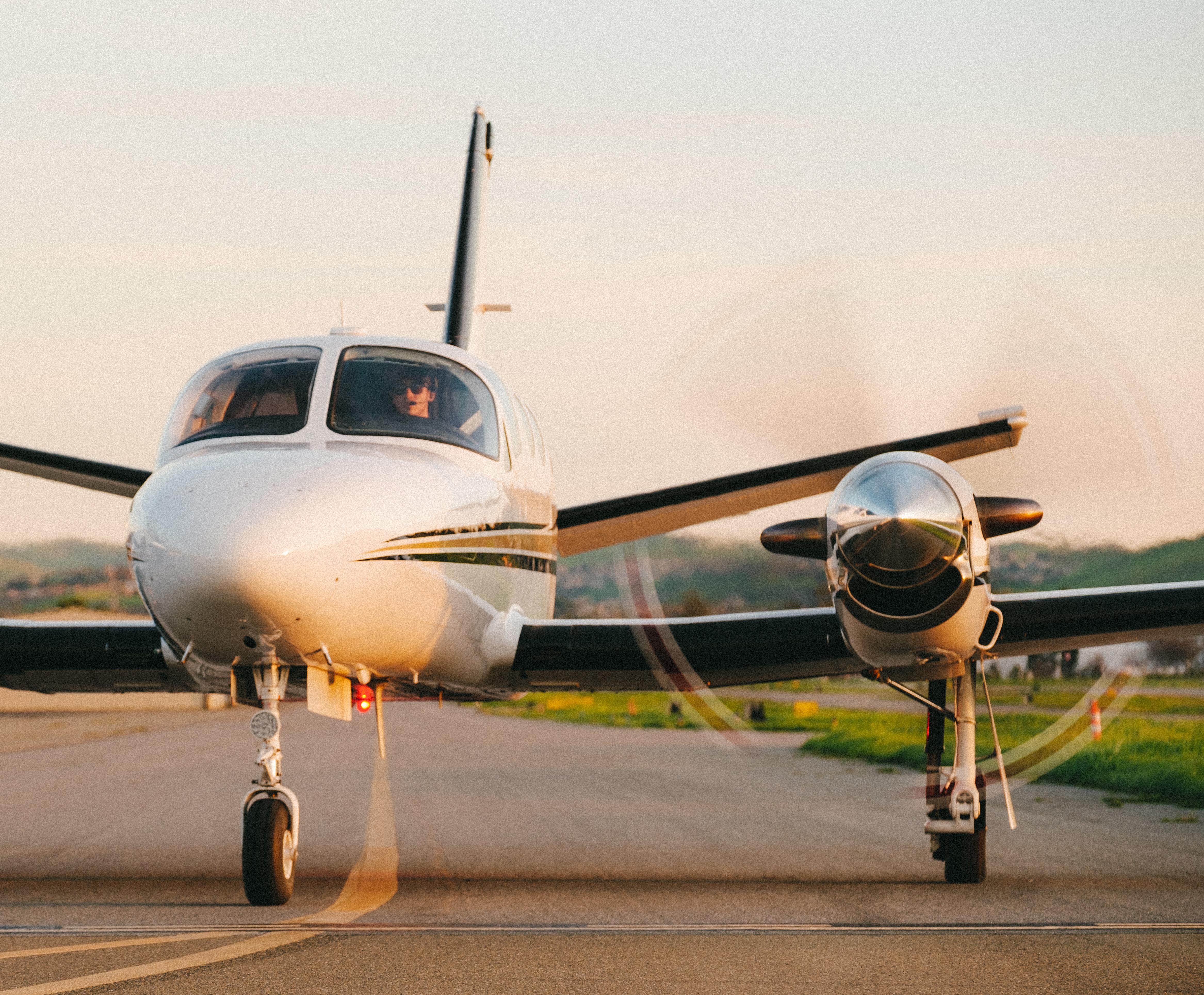small white plane with black and gold stripes sitting on runway; propellers spinning