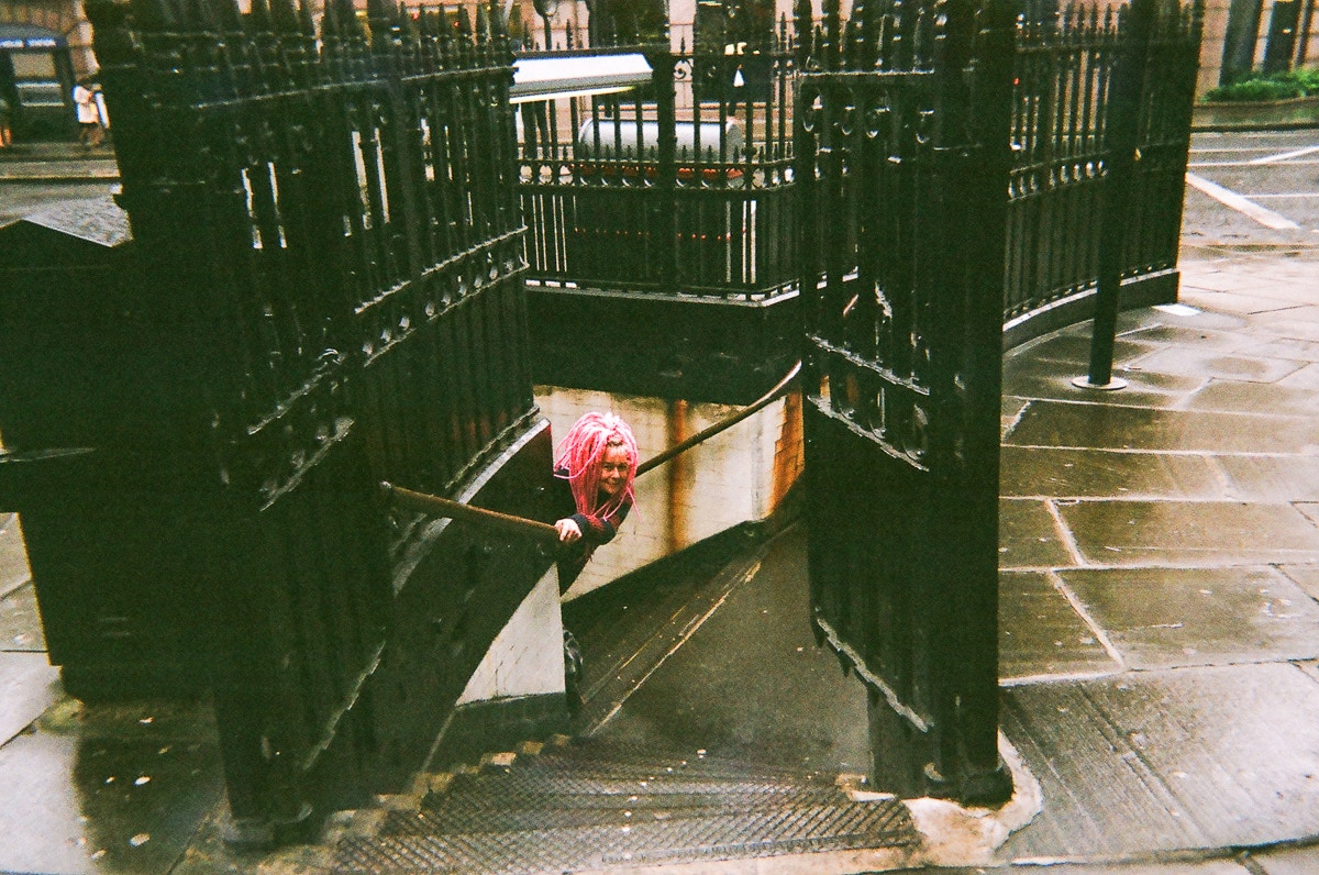 woman with bright pink hair peeks around a stairwell