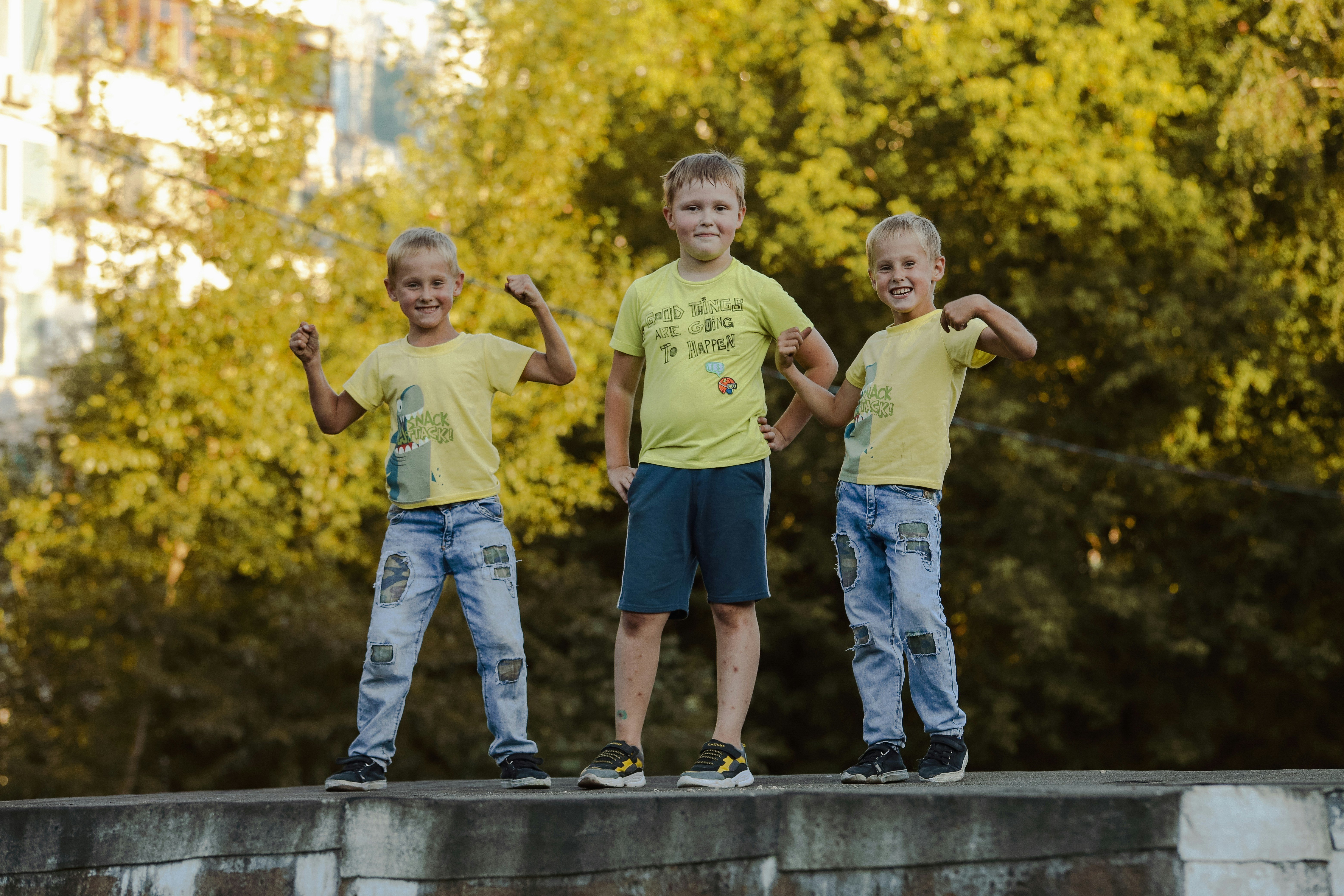 3 young boys stand on concrete next to each other during the day