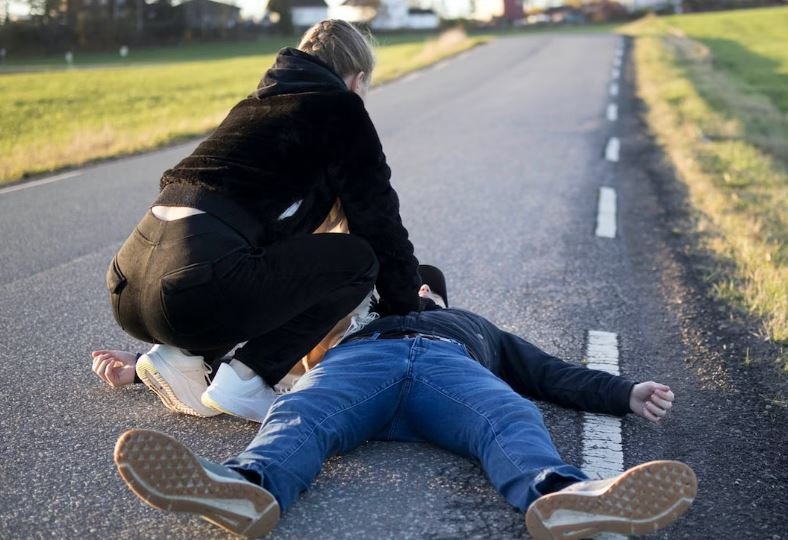 Someone tending to a man collapsed on a roadway