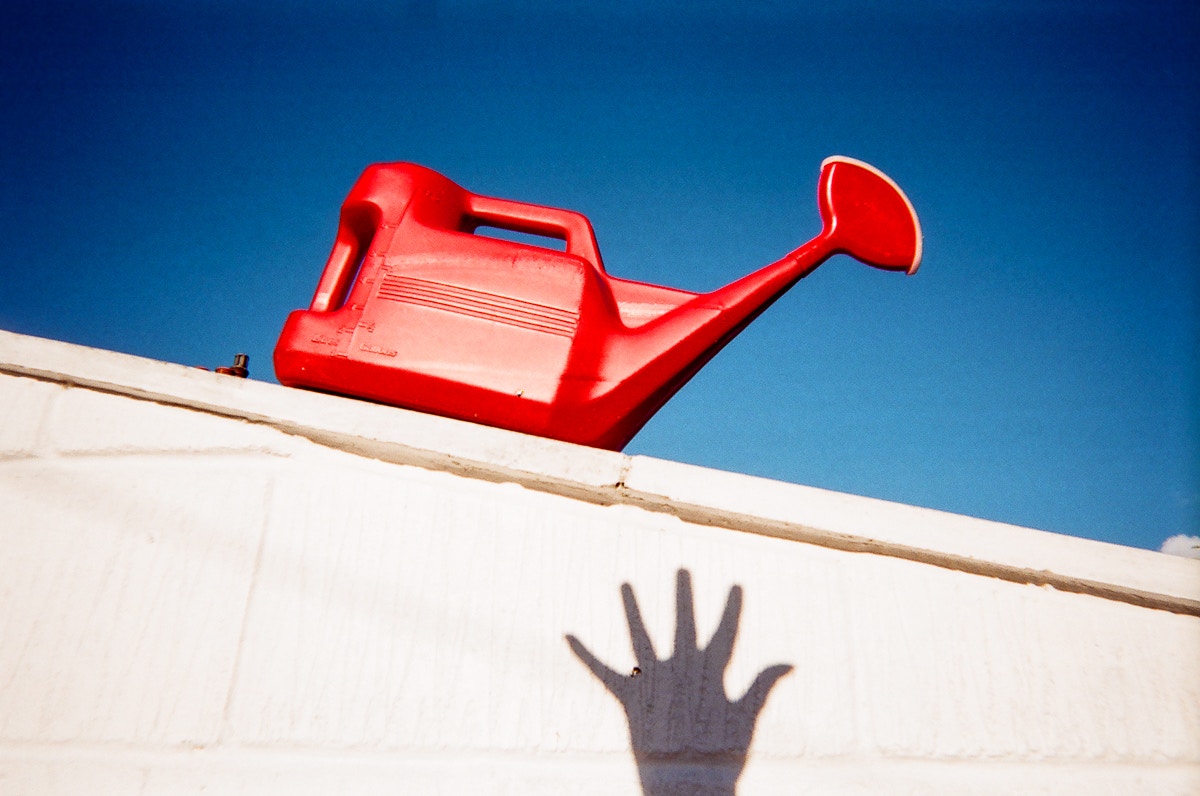 A hand shadow reaches up the wall toward a red water container.