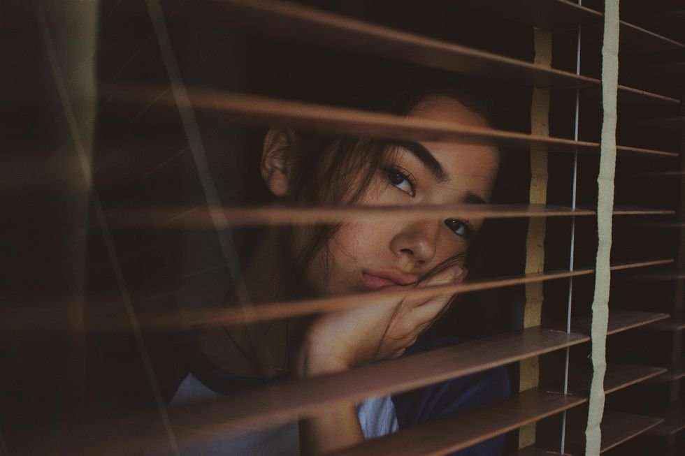 a woman looks through blinds