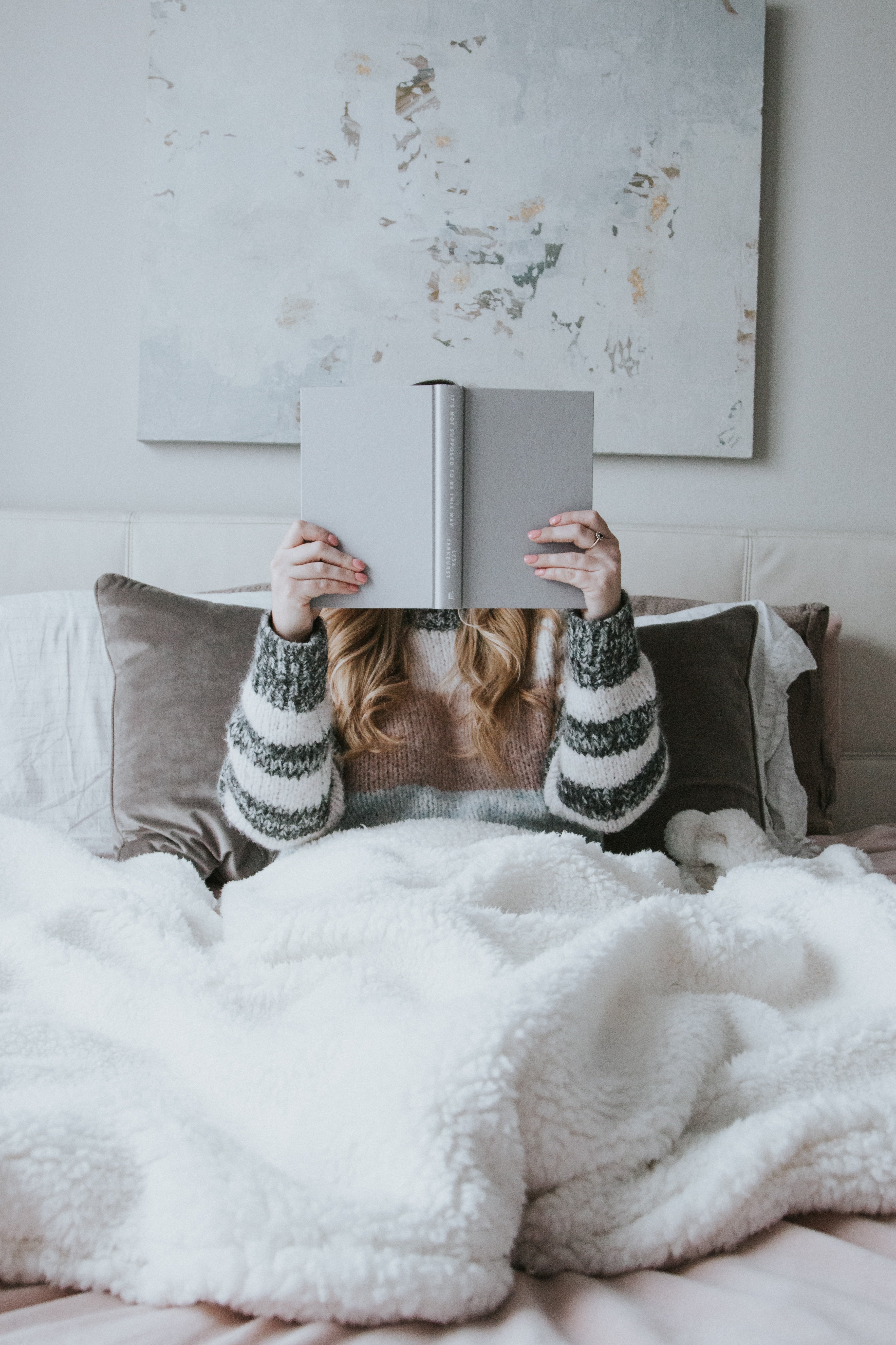 woman reading under a fluffy blanket