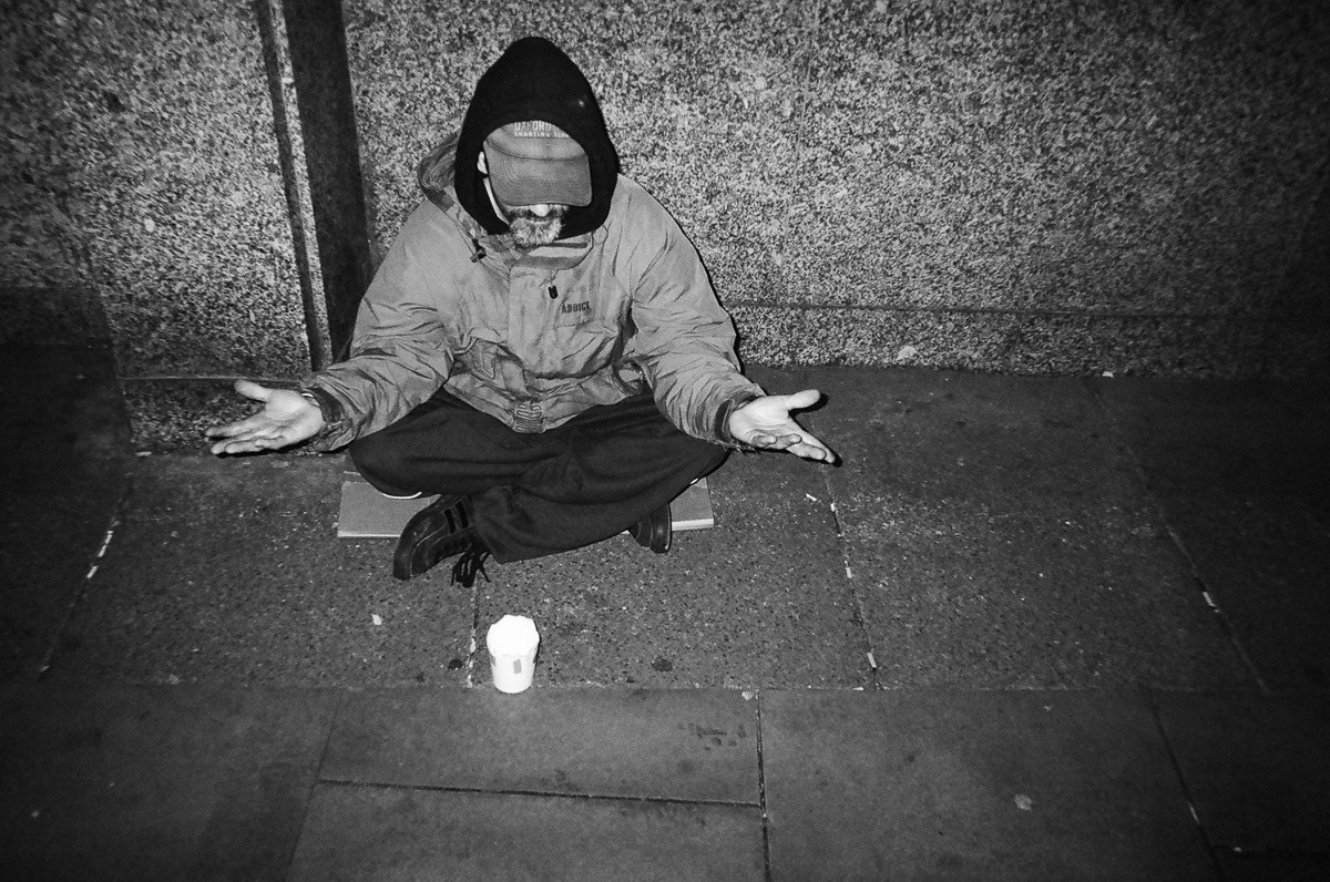 black and white photo of homeless man with hands open sitting on the sidewalk waiting for donations