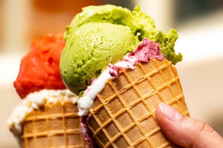 Two waffle cones, one holding green ice cream and one holding red ice cream