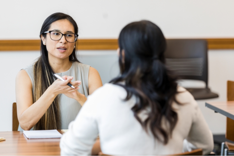 A woman sits across a table from another woman in a professional environment