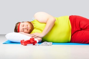 A man in gym clothes lies on a yoga mat with a pillow under his head and appears to be sleeping