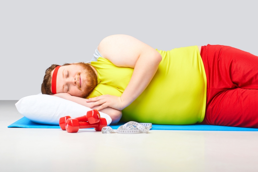 A man in gym clothes lies on a yoga mat with a pillow under his head and appears to be sleeping