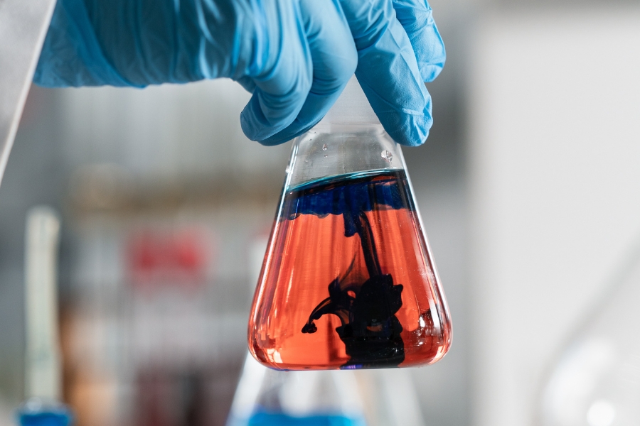 A scientist holds a flask in which blue dye has been dropped into a red liquid