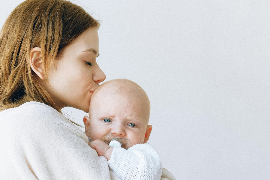 A woman kisses a baby on the top of the head