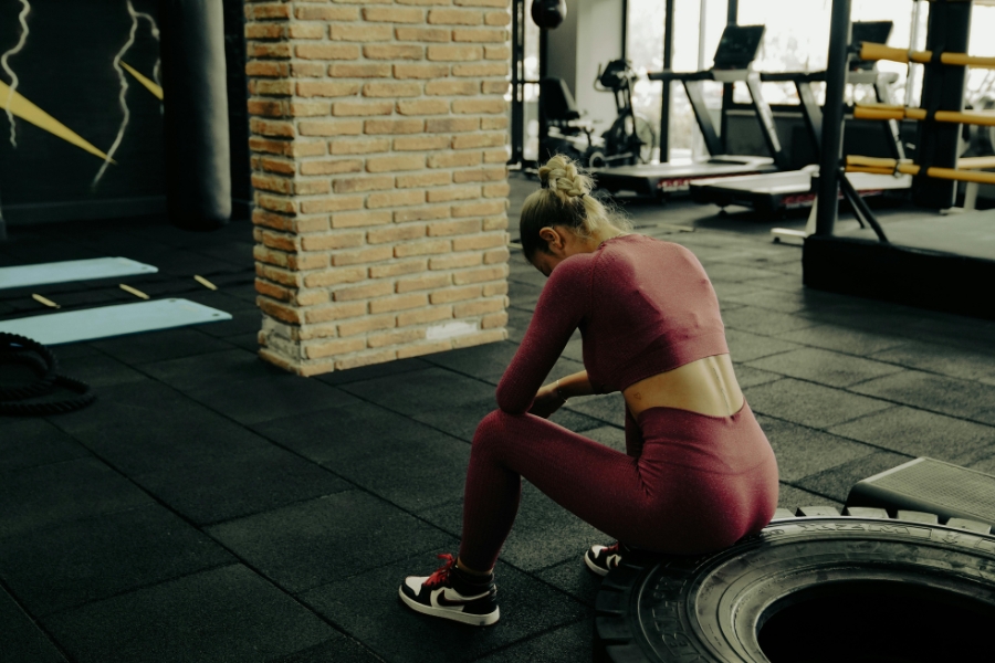 A woman in workout clothes sits on a tire in a gym