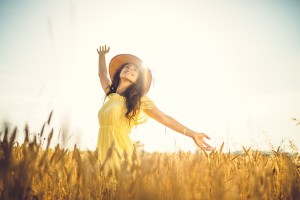 A woman stands in a wheat field looking happy in the sun