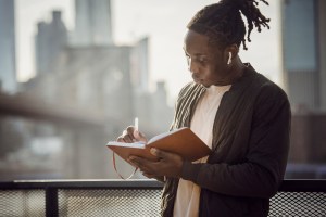 A man stands outside writing in a journal
