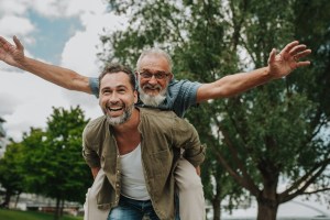An older man is given a piggy back ride by his son, both looking happy and healthy