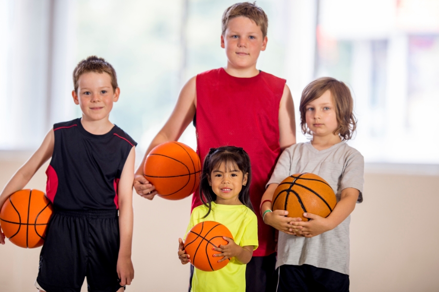 A group of kids of different sizes and ages together holding basketballs