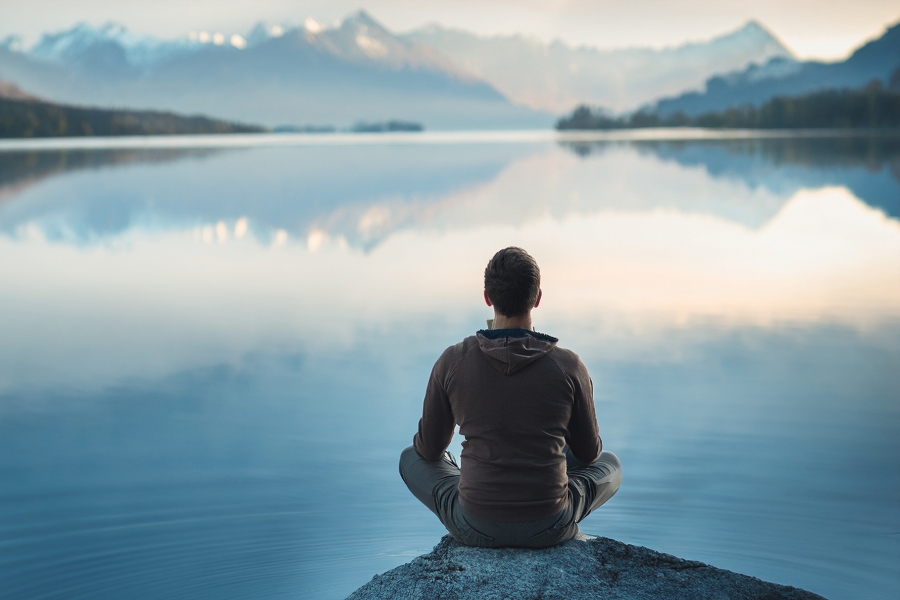 A man sits outside in nature in meditation or contemplation.