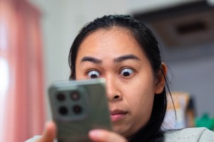 A woman looking at a cell phone with a shocked look on her face