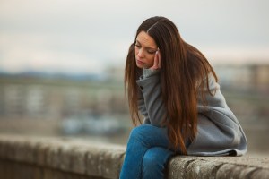 A woman sits on a wall looking lonely