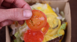 A man holds a sliced tomato over a McDonald's burger box