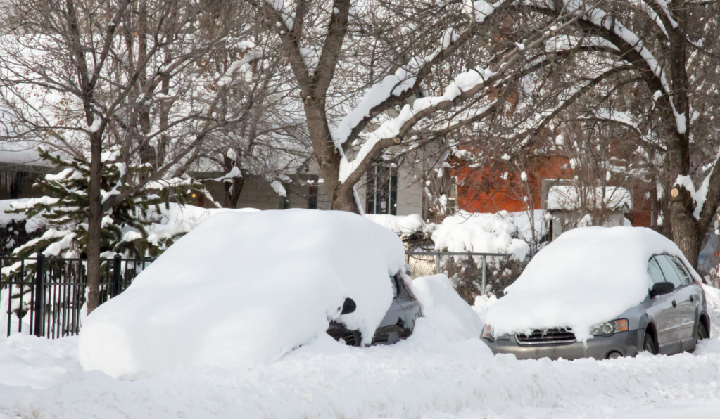 Two cars buried underneath snow parked on the street.