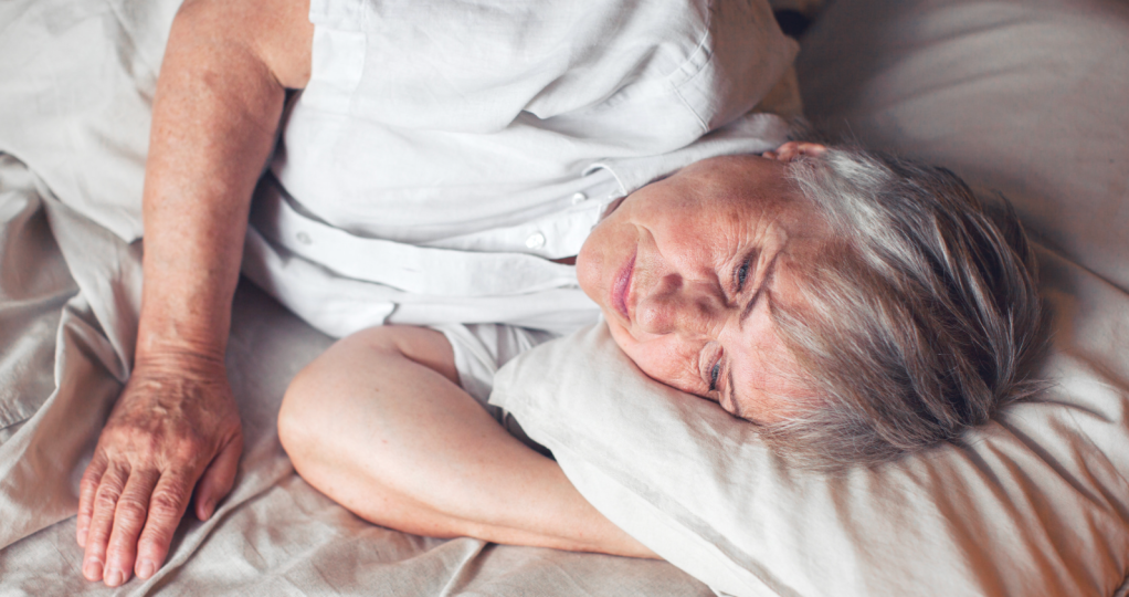 An older woman lays her head down on a pillow.