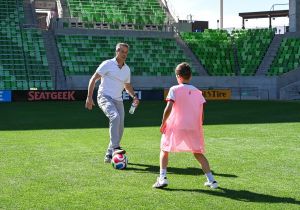 John Harkes coaching a player in a pink jersey on a soccer field.