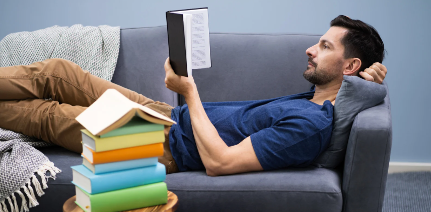 man reading, relaxing with book, stack of books, reading on couch, relaxation
