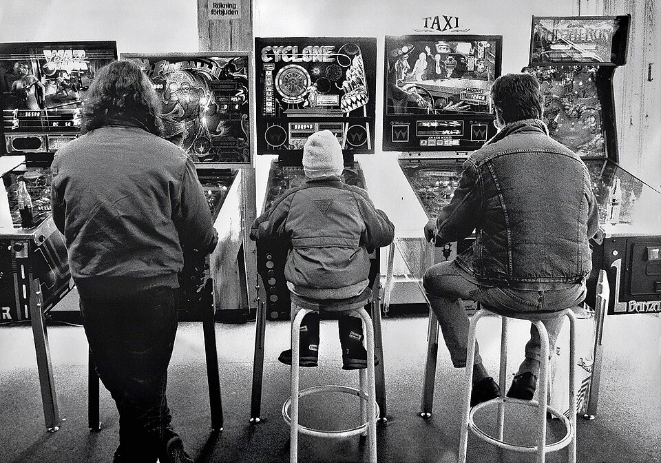 pinball, arcade, two men, one child, stools