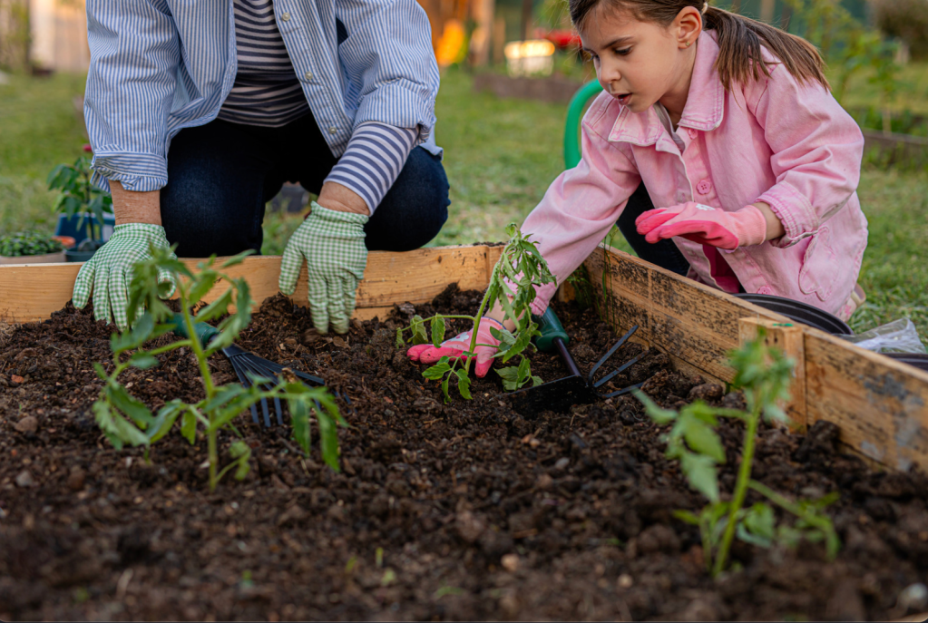 A mother and daughter wearing gloves gardening with their hands in soil.