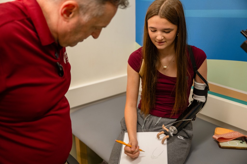Shelby practicing to write with her new prosthetic and Shriners Children's team.