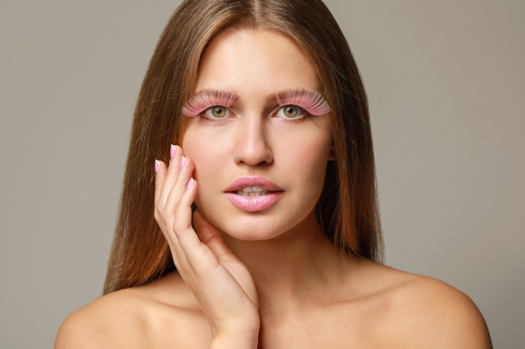 A woman with long brown hair wearing enormous fake peach colored eyelashes.